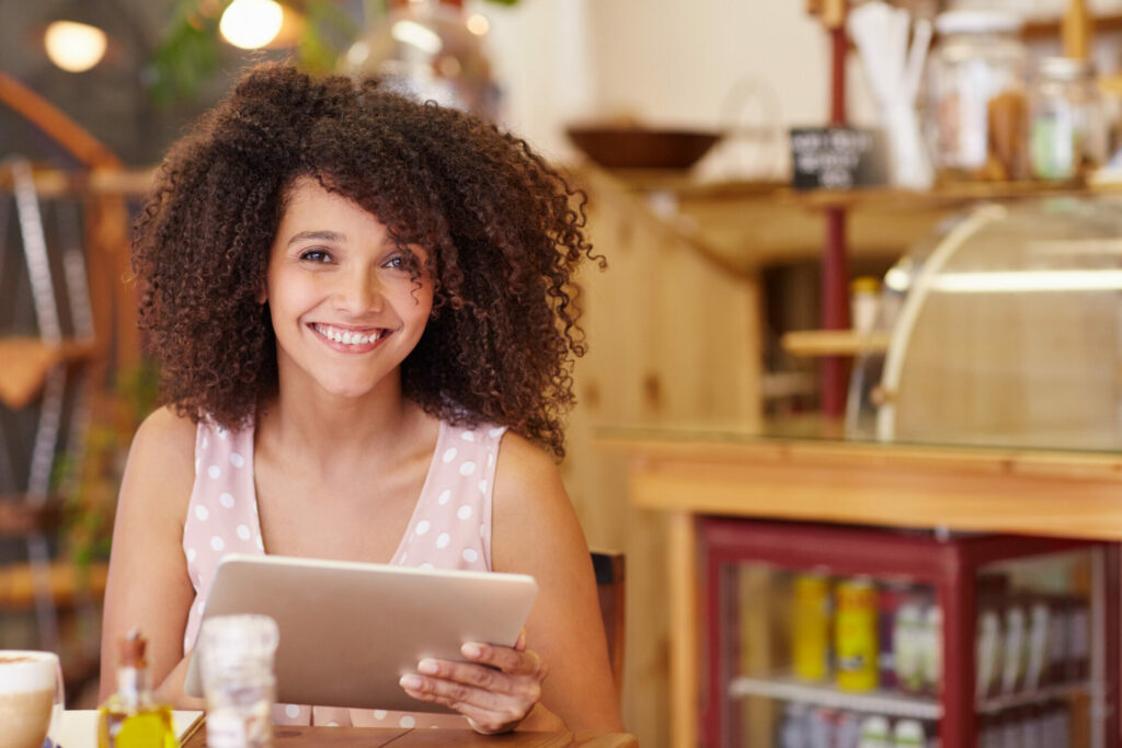 Mixed race woman smiling and holding tablet in a cafe